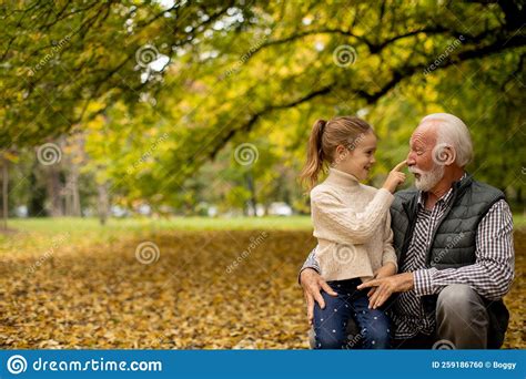 Grandfather Spending Time With His Granddaughter In Park On Autumn Day