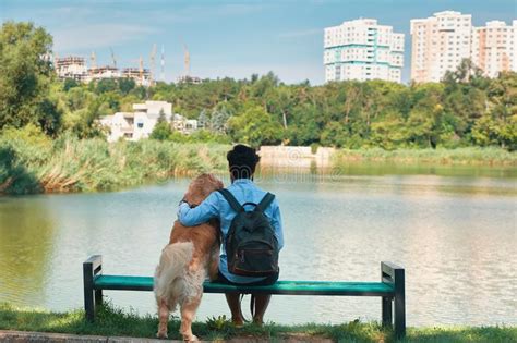 Young Man Sitting With His Dog On The Chair In The Park Enjoyin Stock