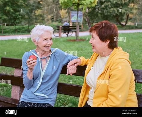 two mature women eating apples on the bench after doing sport exercises in the park healthy