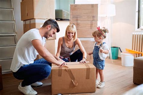 Smiling Parents With Child Moving In New Home Unpacking Boxes Stock