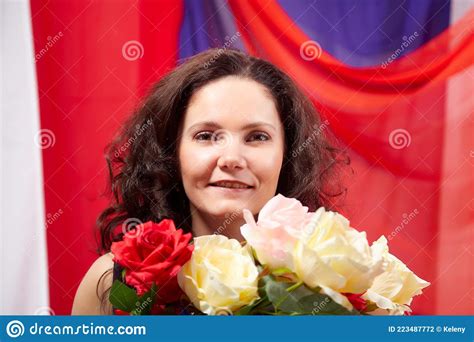 Woman In Blue Dress With Long Brunette Curly Hair And Roses In Hands Indoors With Red And Blue