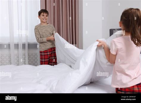 Brother And Sister Changing Bed Linens Together In Bedroom Stock Photo