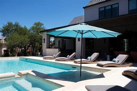 An In Ground Pool And Spa Is Fitted With A Blue Umbrella And Surrounded