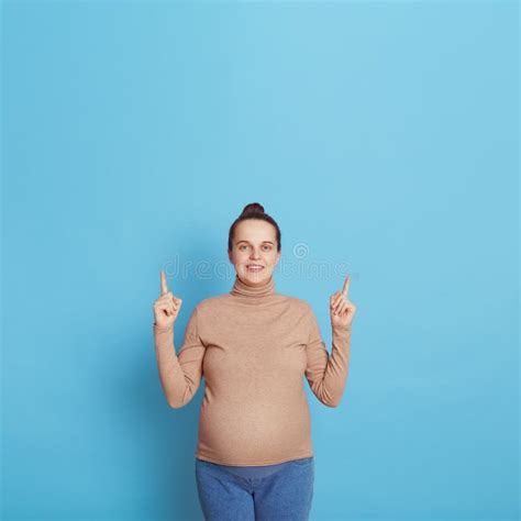 attractive european pregnant woman pointing finger up with both index fingers looks at camera