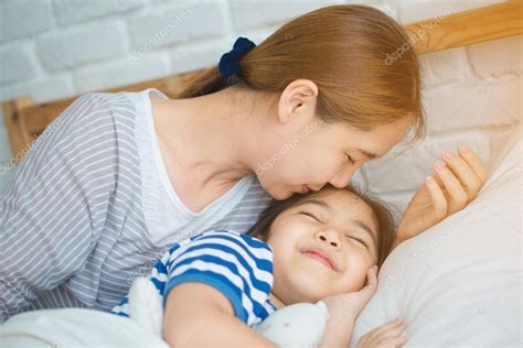 Asian Mother Kissing Her Daughter Goodnight On The Bed Stock Photo By