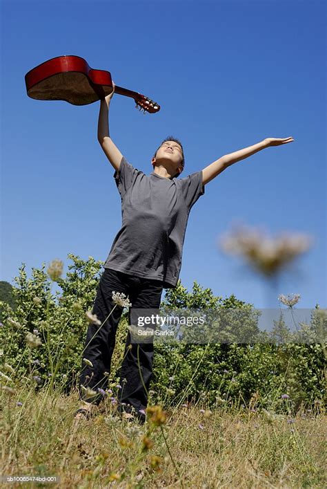 Boy Standing In Meadow Holding Guitar In Outstretched Arms Low Angle