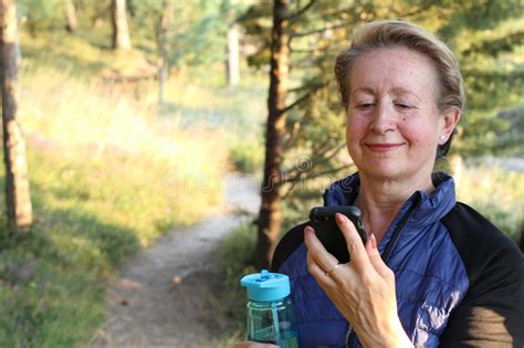 mature athletic woman out training in the woods standing looking at her smart phone as she uses