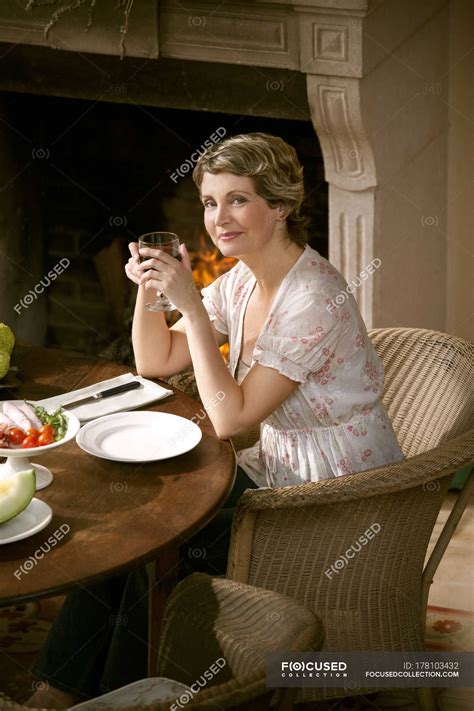 Portrait Of Smiling Mature Woman Sitting At Laid Table Holding Glass Of