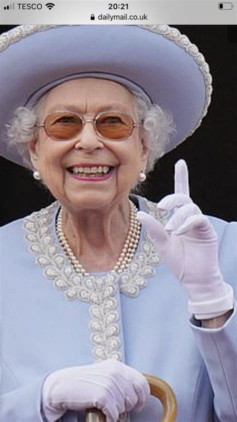 An Older Woman In A Blue Dress And White Hat Is Holding Up A Peace Sign