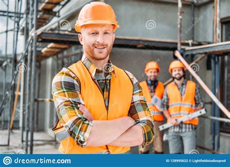 Smiling Builder Standing At Construction Site With Crossed Arms While ...