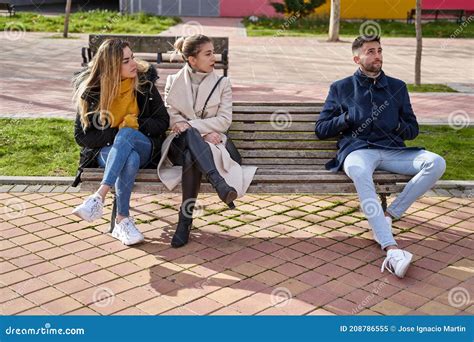 Two Blonde Girls Sitting On A Bench Next To A Guy They Are Looking At Each Other Stock Image