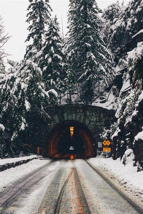 A Snow Covered Road Going Into A Tunnel With Trees On Both Sides And