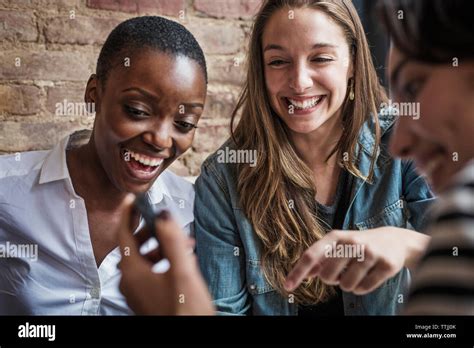 Woman Showing Smart Phone To Friends While Sitting In Cafe Stock Photo