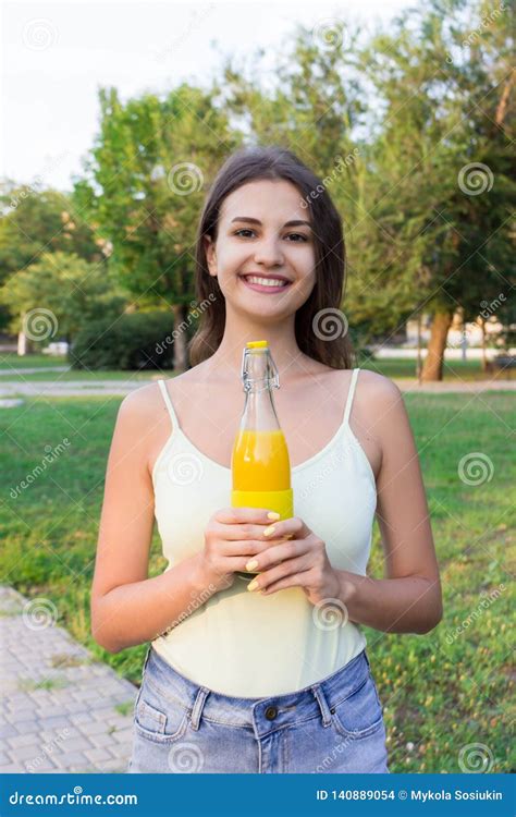 Cute Girl Is Having A Walk In The Park Holding A Bottle Of Orange Juice In A Sunny Wam Day Stock