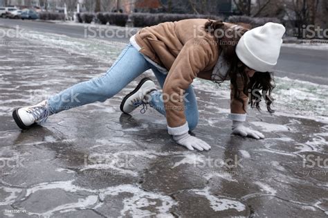 Young Woman Trying To Stand Up After Falling On Slippery Icy Pavement