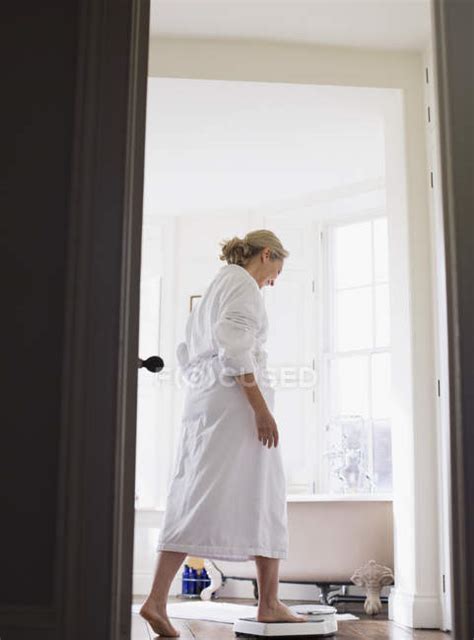mature woman in bathrobe stepping on bathroom scale — healthy living self improvement stock