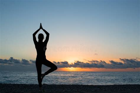 Silhouette Of Person Doing Yoga On The Beach At Sunrise Stock Photo