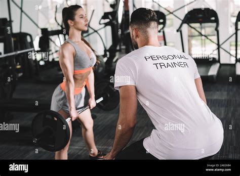 Back View Of Personal Trainer Looking At Attractive Sportswoman Lifting