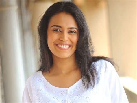 a smiling woman with long dark hair wearing a white shirt and blue jeans standing in front of a