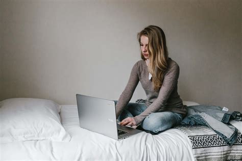 Computer Woman Typing On Macbook Pro While Sitting On Bed In Room