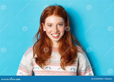 Close Up Of Cute Redhead Girl In Sweater Smiling Happy At Camera Standing Against Blue