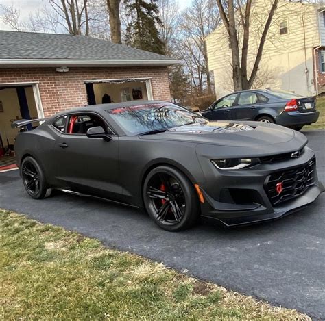 A Gray Camaro Is Parked In Front Of A Garage With Two Cars Behind It