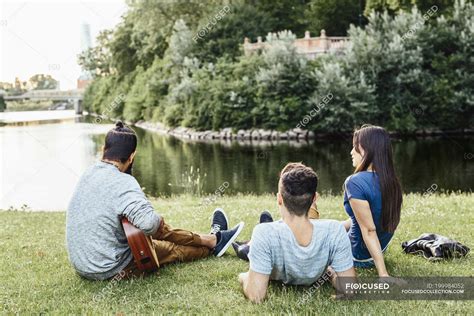 Three People Relaxing In Park With Guitar — Male Sitting Stock Photo