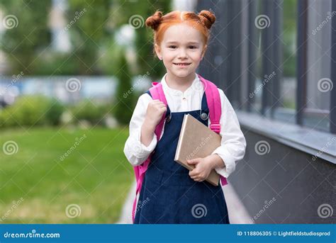 Adorable Cheerful Redhead Schoolgirl Holding Book And Smiling Stock