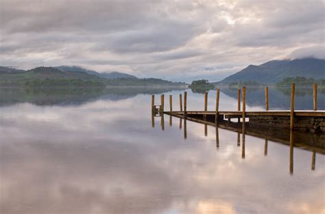 Online Crop Wooden Dock Reflecting Over Calm Body Of Water With