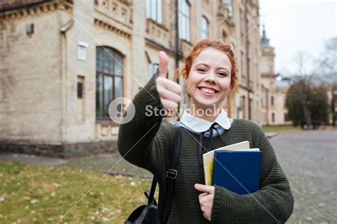 Portrait Of A Smiling Pleased Female Student Holding Books And Showing