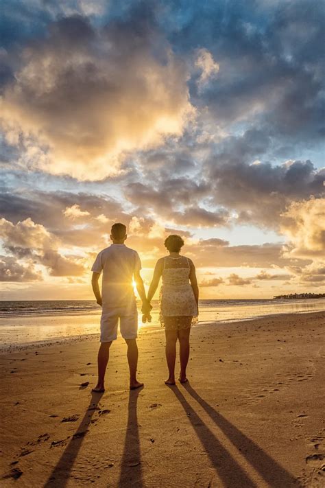 Back View Photo Of Couple Standing On The Beach Looking At The Horizon
