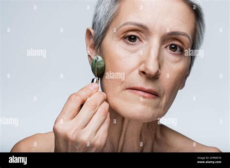 Close Up Of Mature Woman Massaging Face With Jade Roller Isolated On