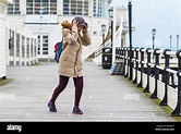 Woman struggling to walk into the wind while holding her hat on ...