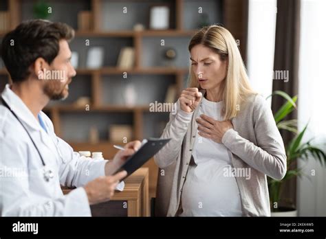 Sick Pregnant Woman Coughing During Meeting With Doctor In Clinic Stock