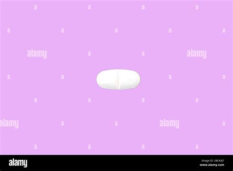 An elongated medical pill with a dividing notch on a pink background