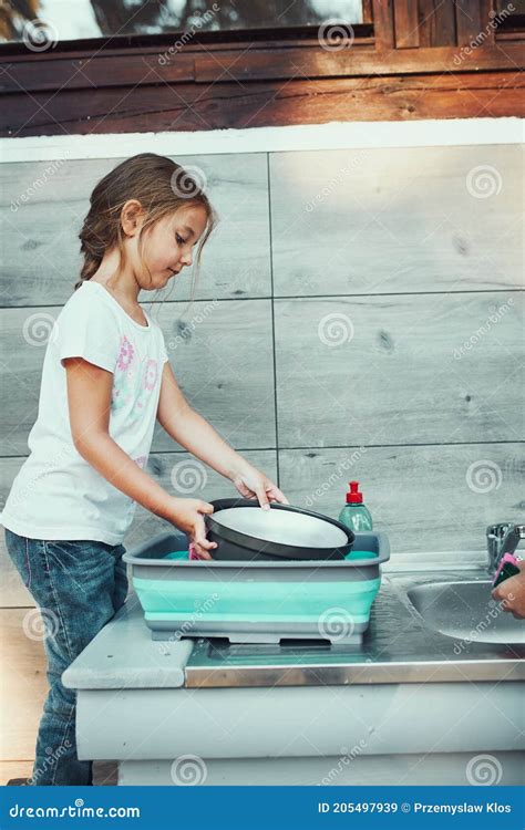 Teenager Girl Washing Up The Dishes Pots And Plates With Help Her