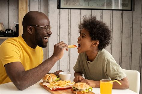 pai e filho comendo hambúrgueres e batatas fritas juntos foto premium