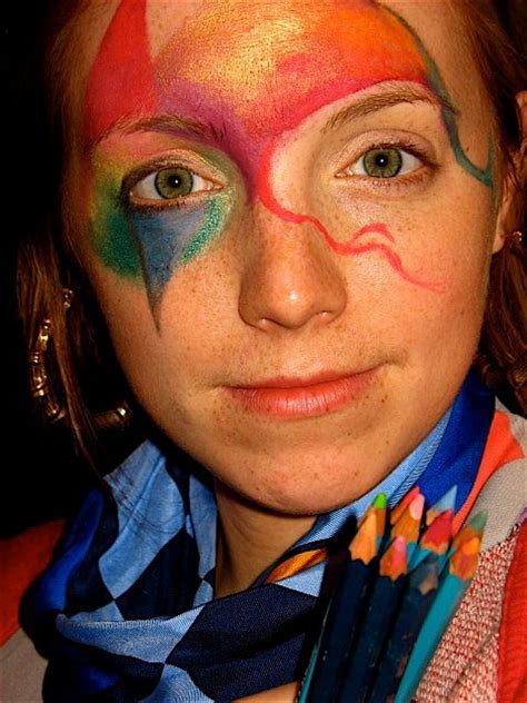 A Woman With Her Face Painted In Rainbow Colors And Holding Several Crayon Pencils