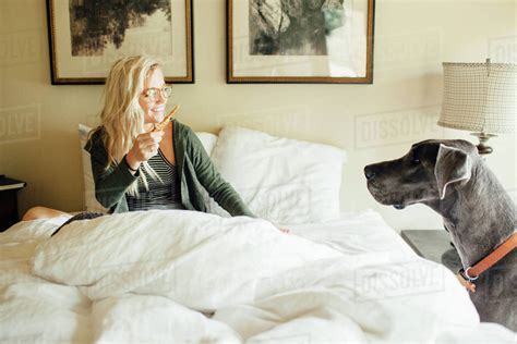 Smiling Woman With Food Looking At Great Dane While Sitting Bed Stock