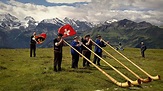 People in traditional Swiss costume blow Alphorns with a Swiss flag and ...