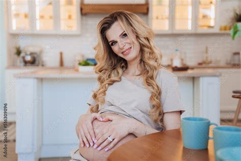 Adorable Pregnant Blonde Swedish Woman Sitting At Table At Kitchen