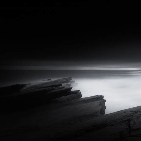 A Black And White Photo Of The Ocean At Night With Rocks In The Foreground