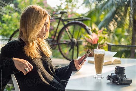 woman sitting in a coffee shop checking her phone del colaborador de stocksy jovo jovanovic