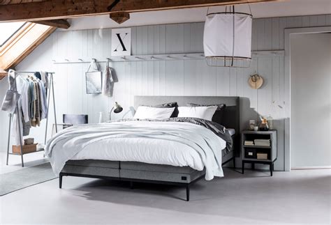 A Bedroom With A Bed Dresser And Clothes Hanging On The Wall In Front