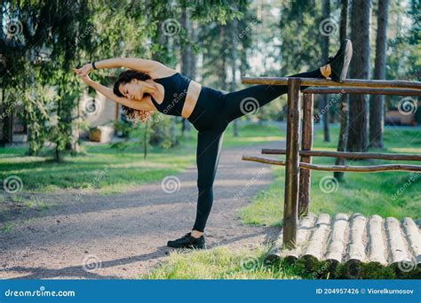 Outdoor Shot Of Active Slim Young Woman Does Stretching Exercise Leans