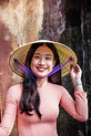 A young Vietnamese woman in a traditional Ao Dai dress and conical hat ...