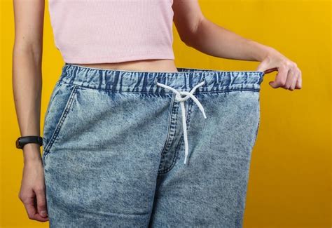 Conceito de perder peso mulher em jeans muito grandes em um fundo amarelo do estúdio cortar