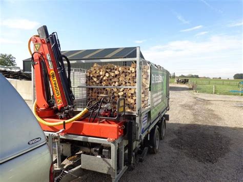 A Truck With Logs In The Back Parked Next To A Car