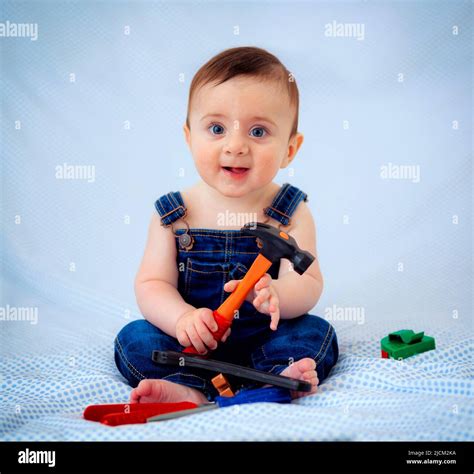 6 Month Old Baby Boy Dressed In Denim Overalls While Playing Tool