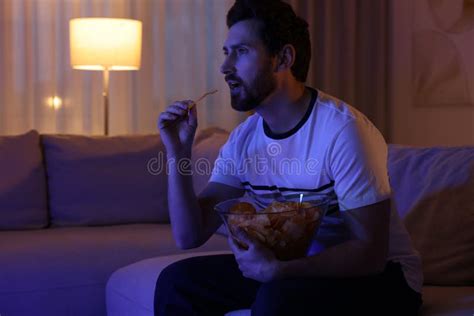 Man Eating Chips And Drinking Beer While Watching TV On Sofa At Night